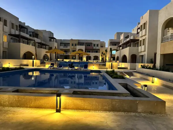 The pool lit at dusk, with the residences behind it